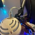 A white spherical microphone with ventilation grilles mounted on an adjustable boom arm in a room with blue LED lighting
