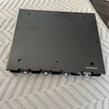 Black electronic device or mounting plate with multiple holes and connectors along the bottom edge, placed on a white textured surface