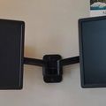 Two Dell computer monitors mounted on a dual monitor arm against a white wall