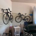 Garage interior with two bicycles mounted on wall hooks above a utility sink, with a car and surfboards visible