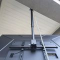 A ceiling-mounted monitor or display screen with adjustable arm and cables in what appears to be an office or medical facility with white ceiling panels