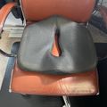 Gray ergonomic seat cushion with cutout opening placed on brown leather office chair