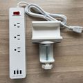 White power strip with multiple outlets and USB ports, connected to a desk clamp mount on wooden surface