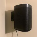 Black cylindrical speaker mounted on wall with cable visible