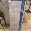 A boxed TV wall mount product (MOUNT-IT! MI-397) with articulating arm and long extension, showing assembly diagrams and product information on the packaging, sitting on a wooden floor next to furniture