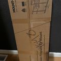 Cardboard box for a Mount-It TV wall mount bracket lying on a wooden floor against a dark wall