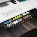 A white desk with an open drawer containing organized office supplies including pencils, pens, sticky notes, paper clips, and other stationery items, with a wireless keyboard and mouse on the desktop surface