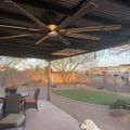 Covered patio with ceiling fan, outdoor dining furniture, and desert landscaping with artificial turf lawn and a white dog