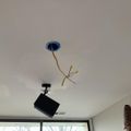 A ceiling with exposed electrical wires hanging from a blue junction box and a black projector mounted nearby