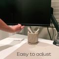 Person adjusting height of black computer monitor on white desk with pencil holder and window blinds in background