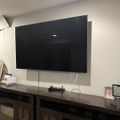 A large flat-screen TV mounted on a white wall above a dark wooden media console with cabinet doors and decorative items