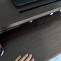 A person's hand resting on a dark wooden desk surface with a laptop and smartphone visible on the desk above