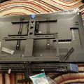 Back view of a disassembled flat screen TV or monitor lying face-down on a striped rug, showing internal mounting brackets and components