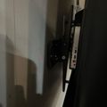A wall-mounted TV bracket attached to a white wall, shown from the side angle in dim lighting