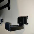 Black wall-mounted shelf or bracket attached to a white wall with another mounting bracket visible in the upper left corner