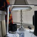 A desk setup with a crystal base table lamp with white shade, black candle, and various items near a window with white blinds