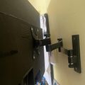 A flat screen TV mounted on a wall bracket with cables visible behind it