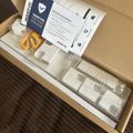 Unboxed keyboard with white keys, documentation, and small accessories in cardboard packaging on wooden surface