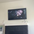 A flat-screen TV mounted on a white wall above a black brick fireplace, displaying what appears to be a movie or TV show scene.