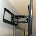 A black adjustable TV wall mount bracket installed on a white wall in the corner of a room