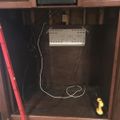 Kitchen cabinet interior showing white electronic device with cables and wiring, with a red measuring tape visible on the left side