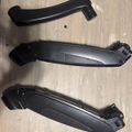 Three black plastic automotive parts or trim pieces laid out on a wooden surface