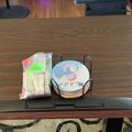 A wooden dining table with a wire basket containing papers and a globe, along with what appears to be a laptop or tablet device