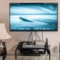 A computer monitor displaying a serene blue ocean scene with a pier sits on a black glass desk, flanked by a table lamp and speaker in a home office setup