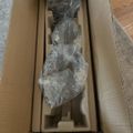 A packaged item wrapped in clear plastic inside an open cardboard shipping box with protective foam padding