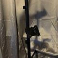 A black adjustable monitor arm mount attached to a pole stand, photographed against a white fabric backdrop with its shadow visible.