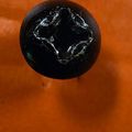 A dark round object with a cross-shaped indentation on top, sitting on an orange surface