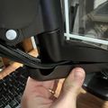Person's hand holding a black plastic piece near a laptop computer on a wooden desk