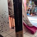 A black book or DVD case titled "Pull Down Fireplace TV Mount" standing upright on a tiled floor in a room with curtains and furniture visible in the background.