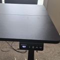 Height-adjustable standing desk with digital control panel showing 46.4 inches, black desktop surface, and cables visible underneath