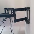 Black adjustable TV wall mount bracket attached to white wall with cables visible