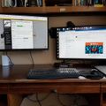 A dual monitor computer setup on a wooden desk with keyboard, mouse, and laptop, displaying web pages on both screens