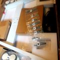 Disassembled furniture parts and hardware laid out in packaging, including wooden panels, metal brackets, and labeled screws in plastic bags