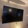 Wall-mounted flat screen TV with visible cables against a white wall with decorative ceiling lighting