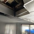 Damaged ceiling with exposed beams and missing tiles in what appears to be a garage or basement area