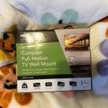 TV wall mount product box labeled "Compact Full Motion TV Wall Mount" sitting on colorful fabric with animal print pattern