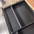 Black plastic storage container with multiple compartments open on a wooden surface