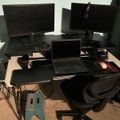 A black desk setup with multiple monitors, a laptop, office chair, and various computer equipment in a home office workspace