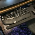 Computer desk setup with black keyboard and mouse on sliding tray beneath monitor