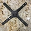 Black TV wall mount bracket with four articulating arms displayed on a speckled granite countertop.