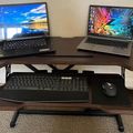 A standing desk setup with two laptops on the upper surface and a keyboard and mouse on the lower pull-out tray