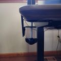 A black adjustable office chair with a round seat and height adjustment mechanism, positioned near a window in a room with wooden flooring