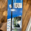 A blue product box for a full-motion TV wall mount lying on a wooden floor, with shipping labels attached and an image of a mounted TV displaying a nature scene on the packaging