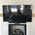 A large flat-screen TV mounted above a white marble fireplace with decorative logs, set against a white shiplap wall
