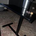 A modern glass-top table with black metal legs on a patterned area rug, with a metallic water bottle and some small objects on the surface