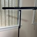 A black adjustable desk lamp with LED lights and control buttons positioned near a window with vertical blinds